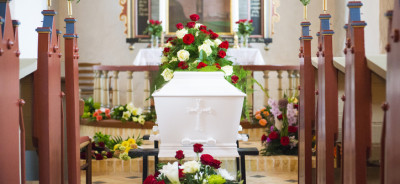 Looking down the church floor, full of flowers. Coffin by the end.