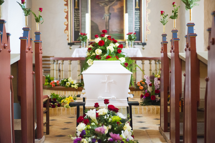 Looking down the church floor, full of flowers. Coffin by the end.